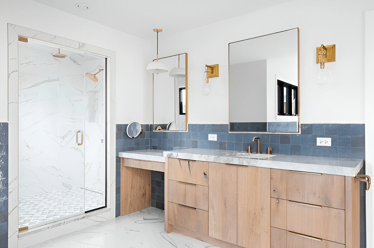 Modern bathroom with wood vanity, marble countertop, glass shower enclosure, and blue accent tiles.