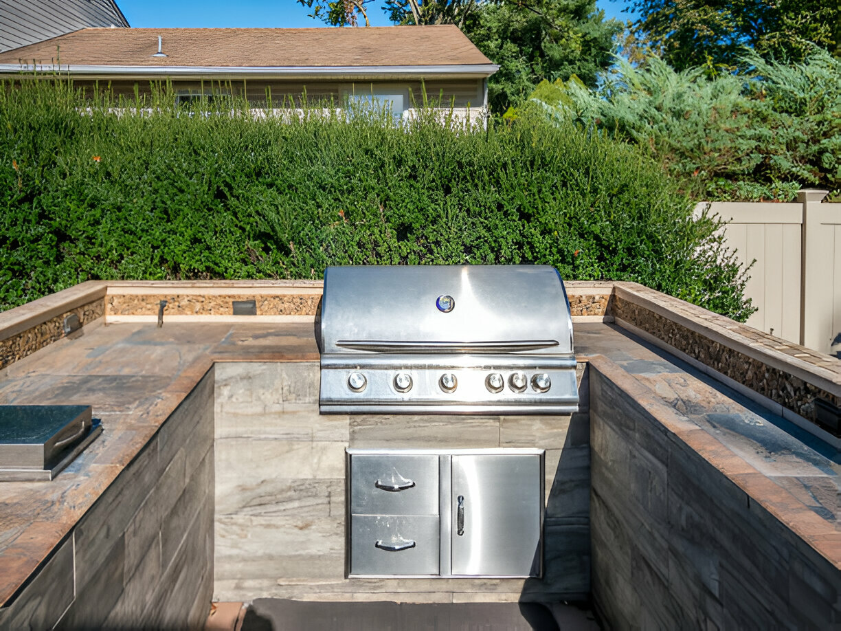 Outdoor built-in grill with stone countertop and privacy hedge 