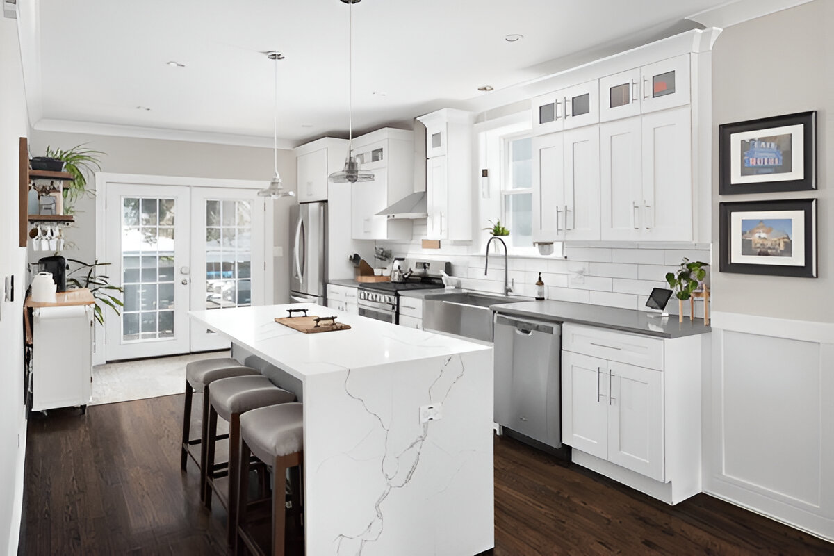 Stylish white kitchen featuring a marble waterfall island, stainless steel appliances, and subway tile backsplash 