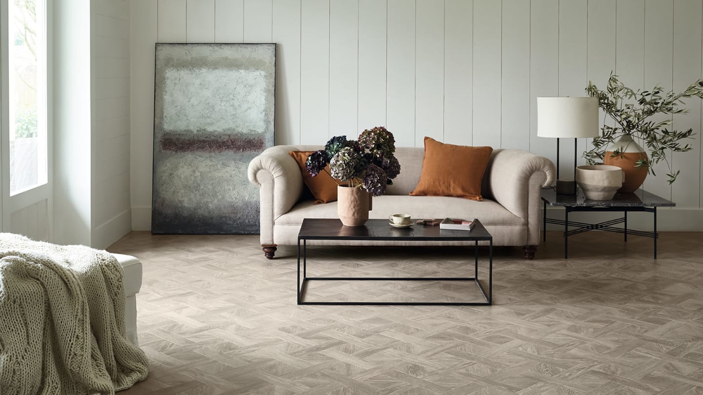 Living room with basketweave patterned oak flooring, beige tufted sofa, rustic coffee table, and warm-toned accessories
