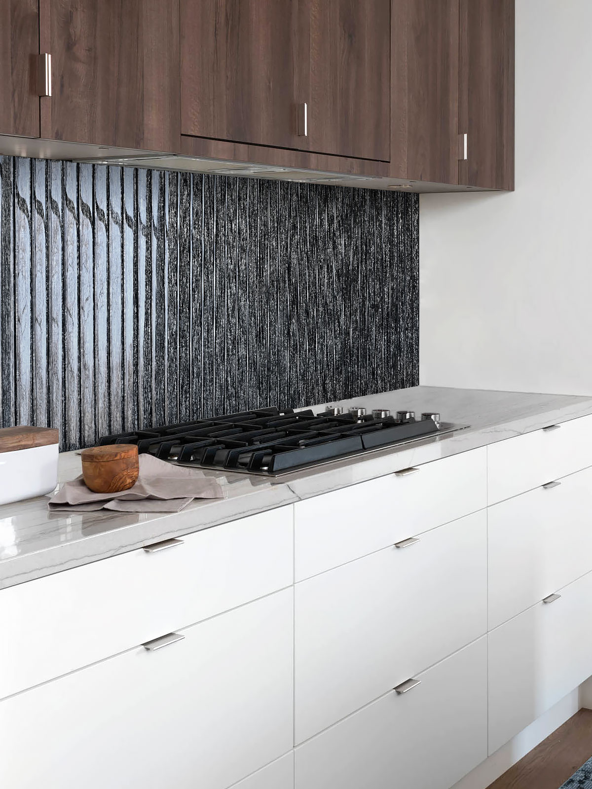 Contemporary kitchen featuring vertical shimmery black glass backsplash tiles, white lower cabinets, and wood upper cabinets