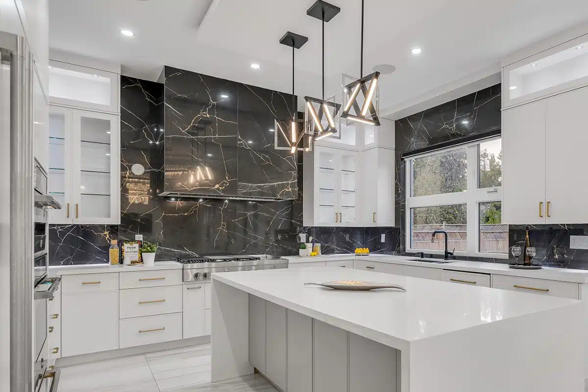 Contemporary kitchen with black marble backsplash, white cabinetry, gold hardware, and pendant lighting over an island