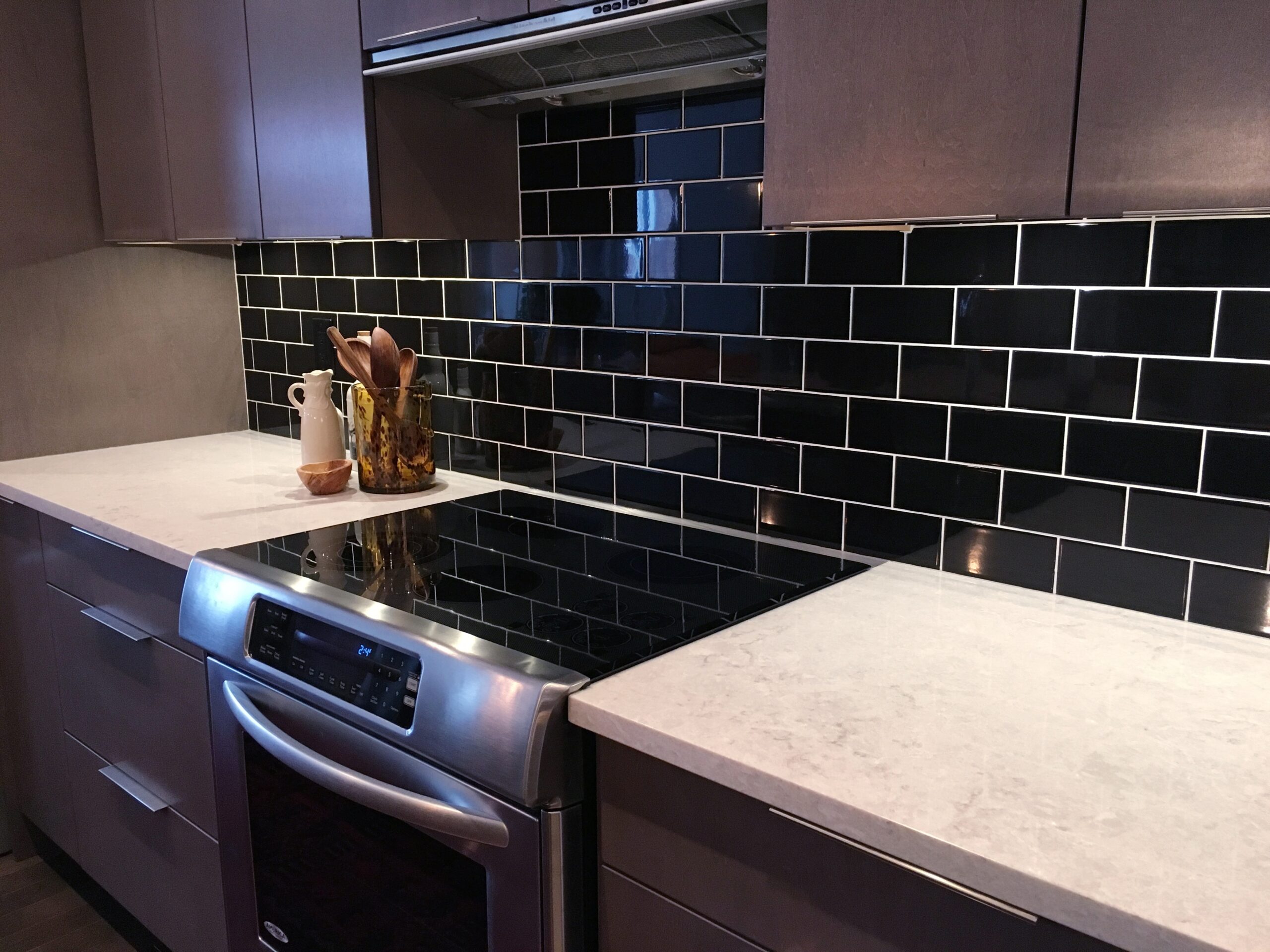 Kitchen with glossy black subway tile backsplash, white quartz countertops, and stainless steel appliances