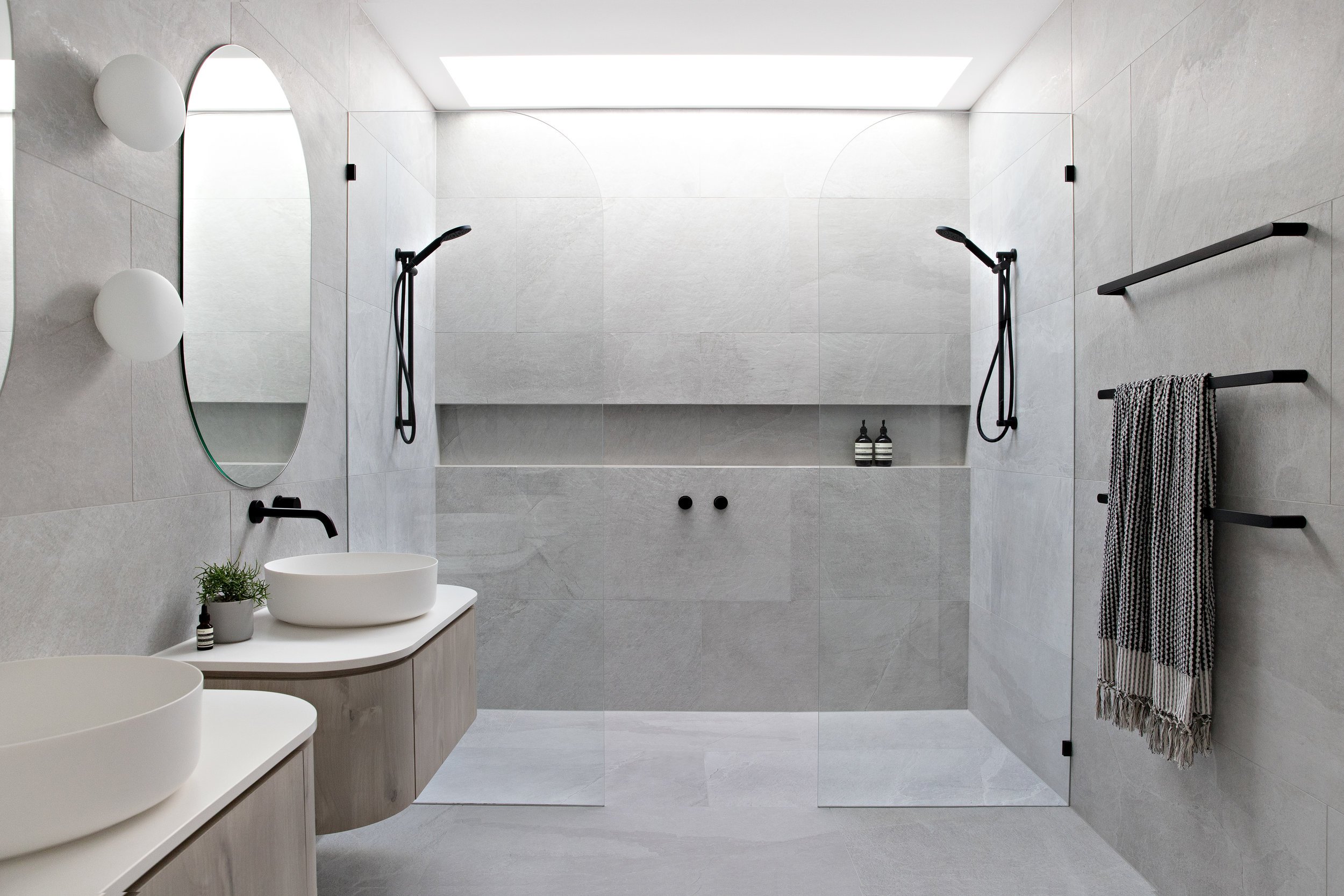 Modern walk-in double shower bathroom with floating vanities, oval mirrors, and matte black fixtures