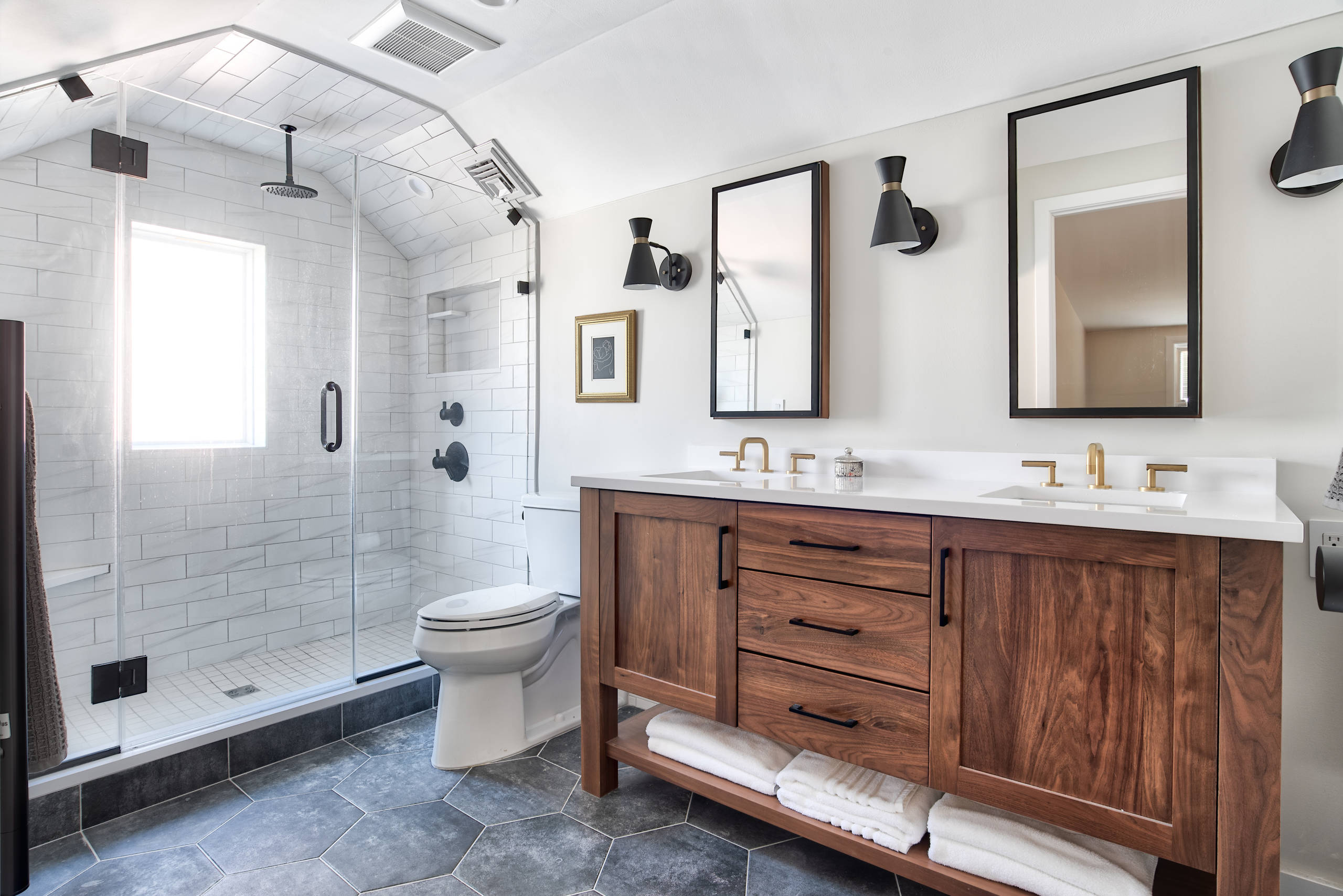 Contemporary bathroom featuring a walnut wood double vanity, hexagonal tile flooring, and a white tiled alcove shower with black fixtures