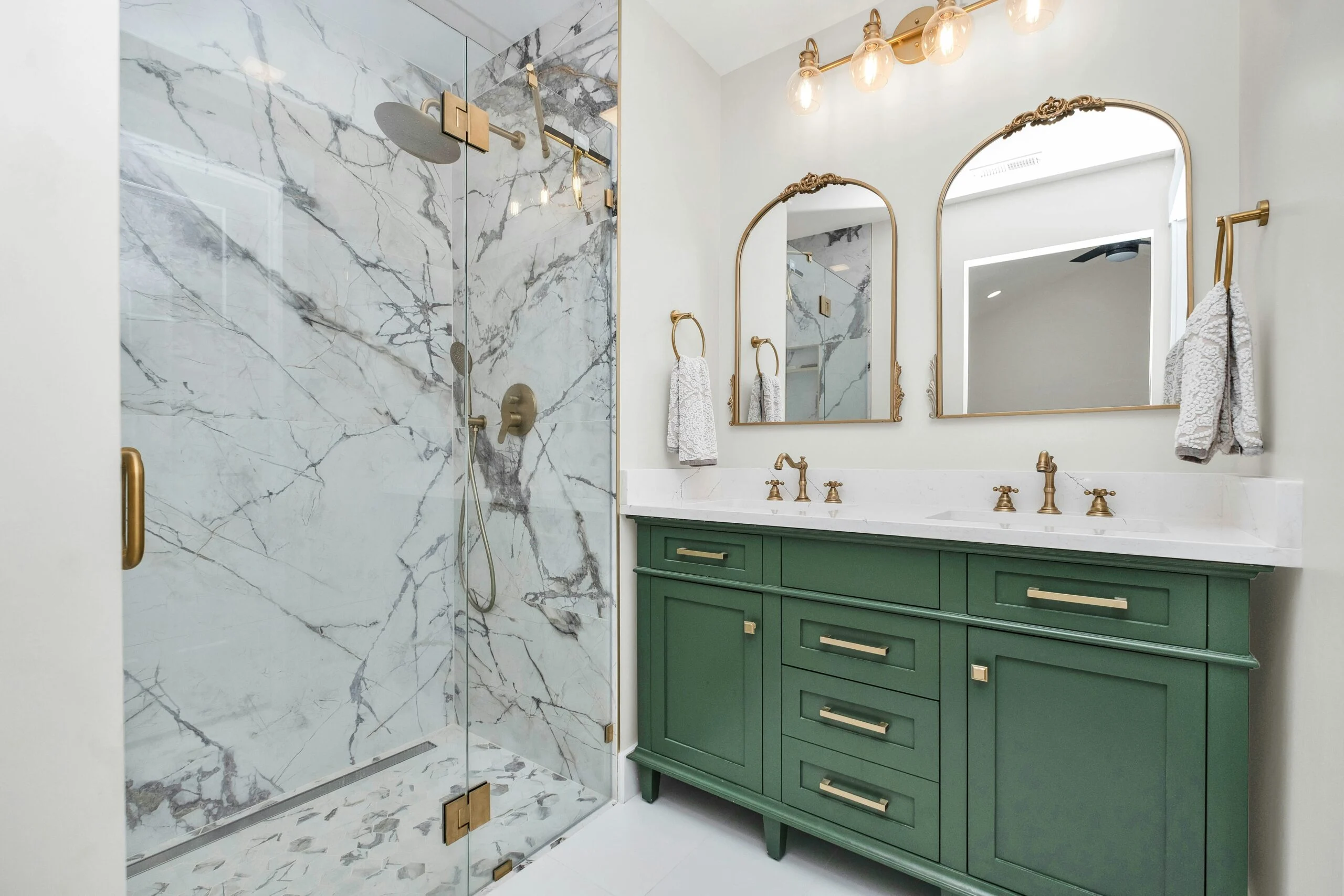 Bathroom featuring green double vanity, gold fixtures, and marble walk-in shower
