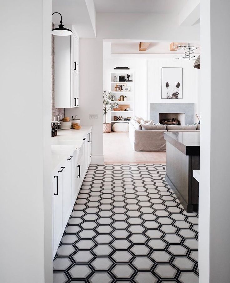 Contemporary kitchen hallway with white cabinetry and striking black-outlined hexagonal tile flooring leading to a cozy open-concept living room.
