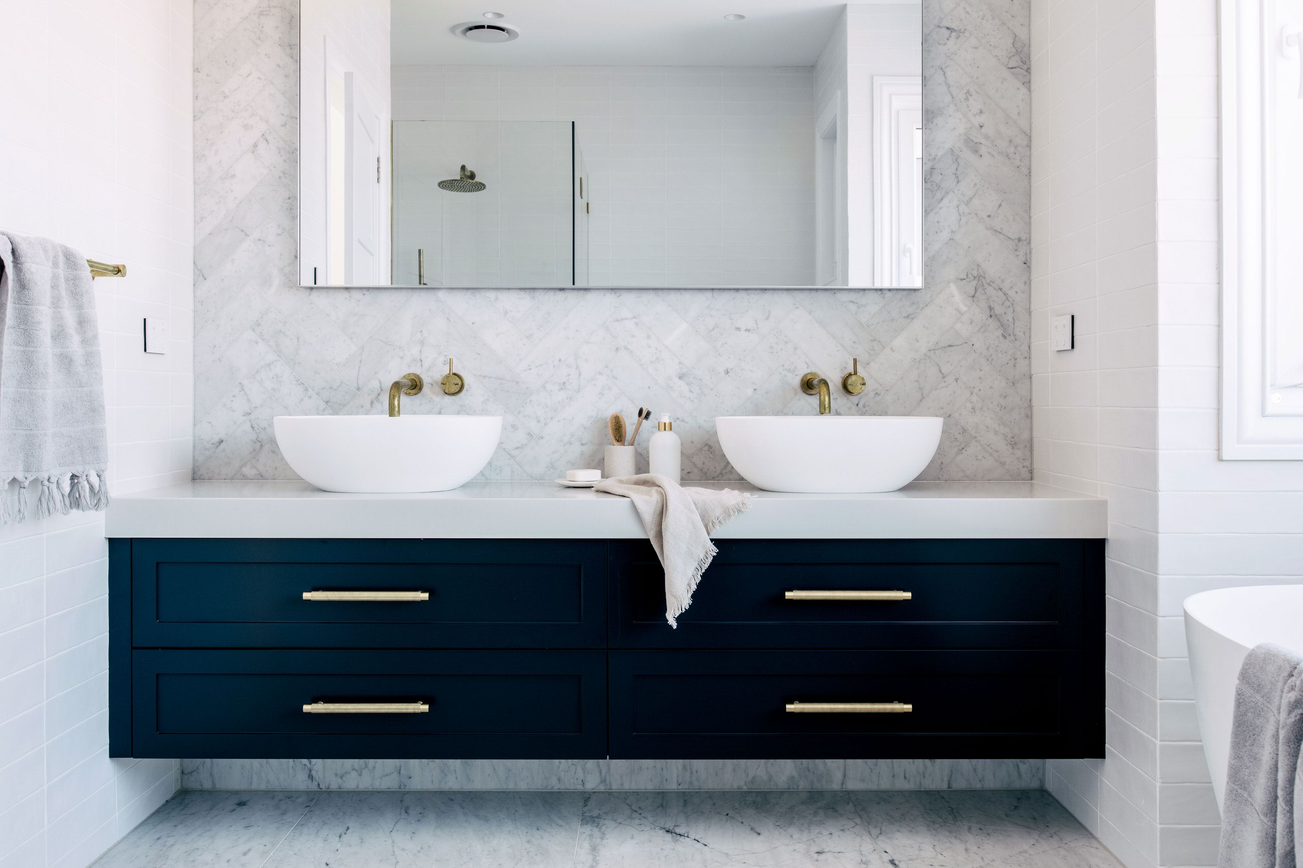 Contemporary bathroom featuring a double vanity with navy blue cabinets, white vessel sinks, and a marble herringbone backsplash