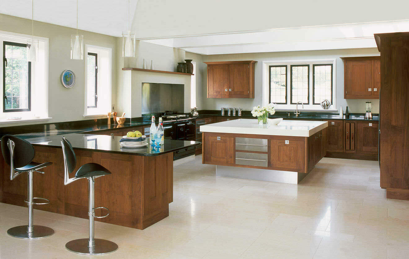 Spacious kitchen featuring dark wood cabinetry, black countertops, a central white island, and polished cream stone flooring.