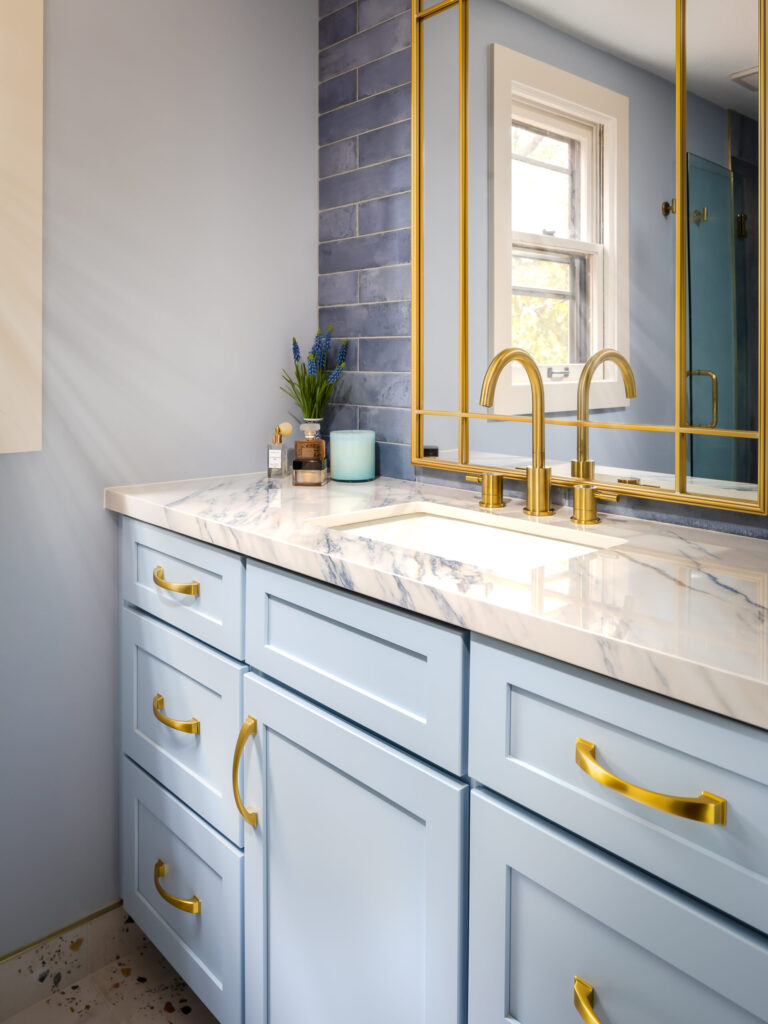 Elegant blue bathroom vanity with gold hardware, marble countertop, and blue tile backsplash beside a large mirror