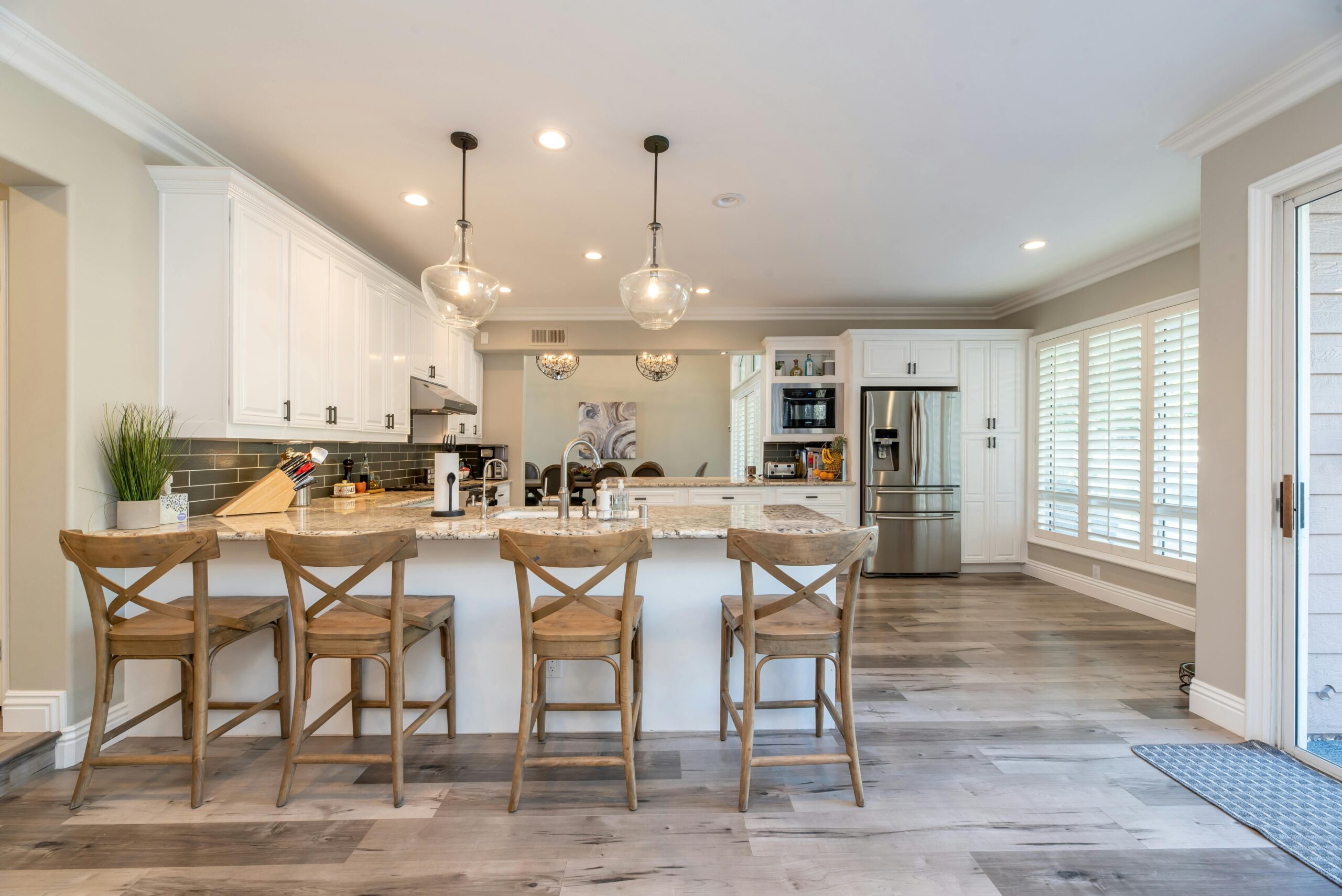 Bright open-concept kitchen with white cabinets, granite countertops, and rustic wooden bar stools.
