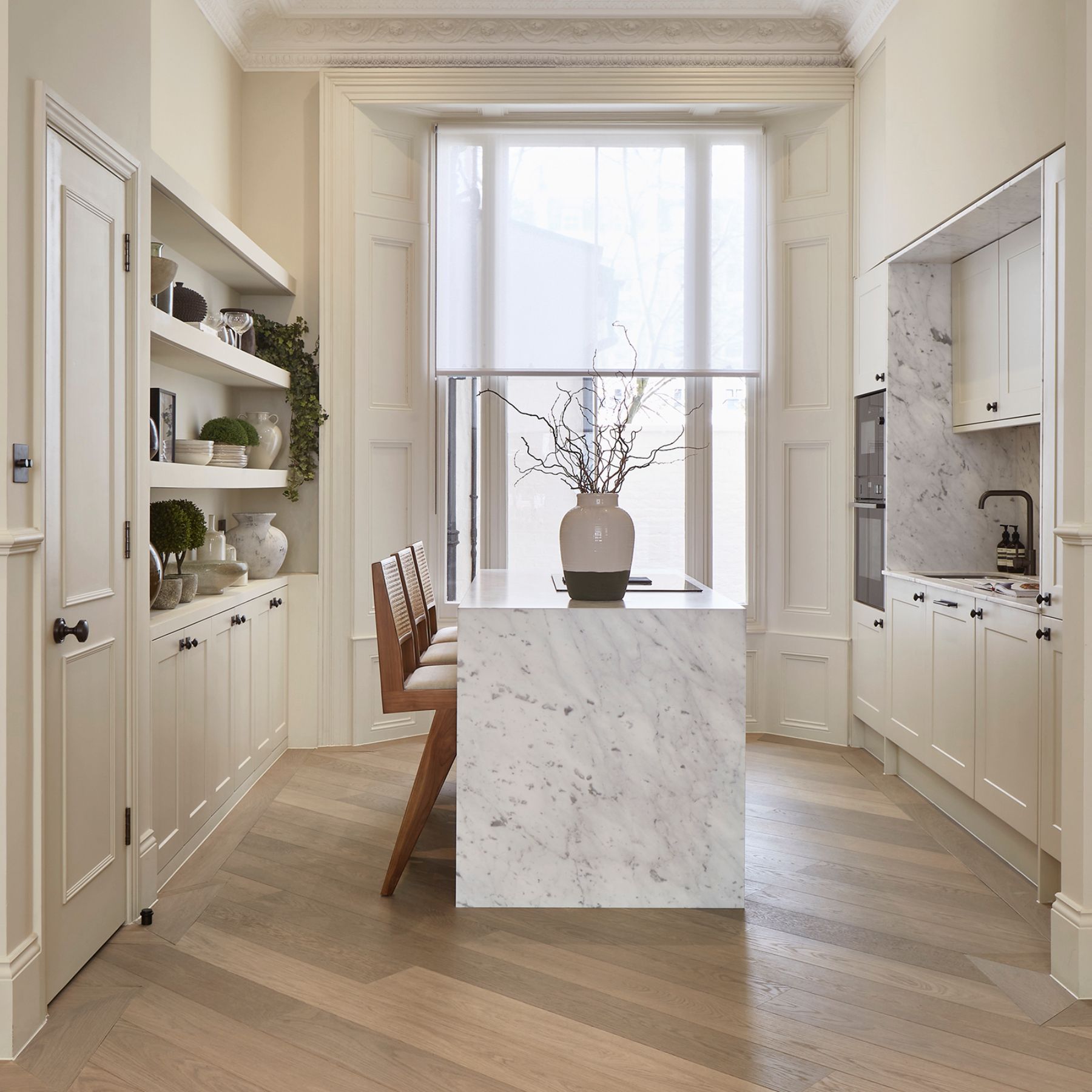 Sophisticated kitchen with chevron wood flooring, marble island, and built-in shelving.
