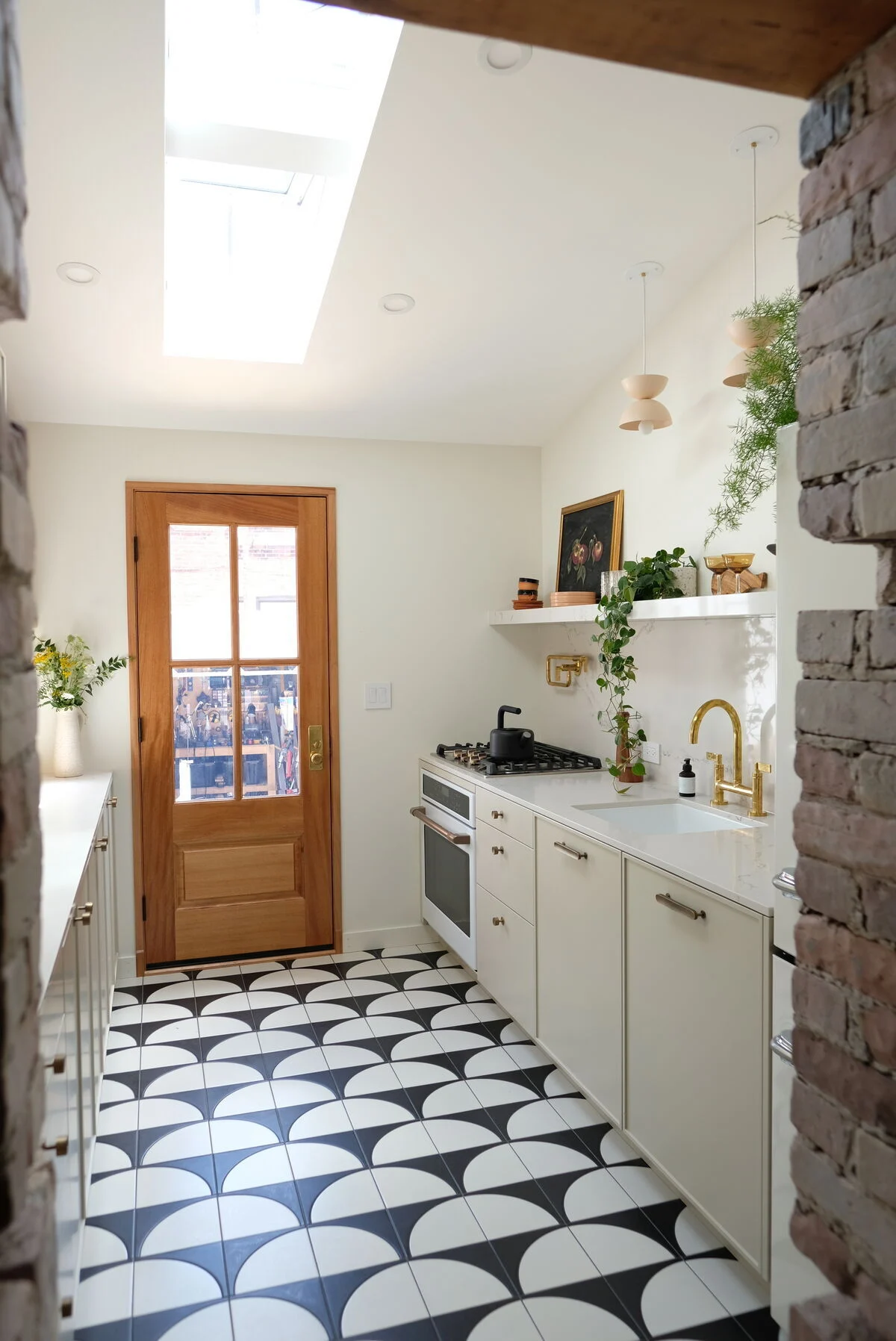 Stylish kitchen interior with black and white semi-circle floor tiles, white cabinets, gold faucet, and wooden door