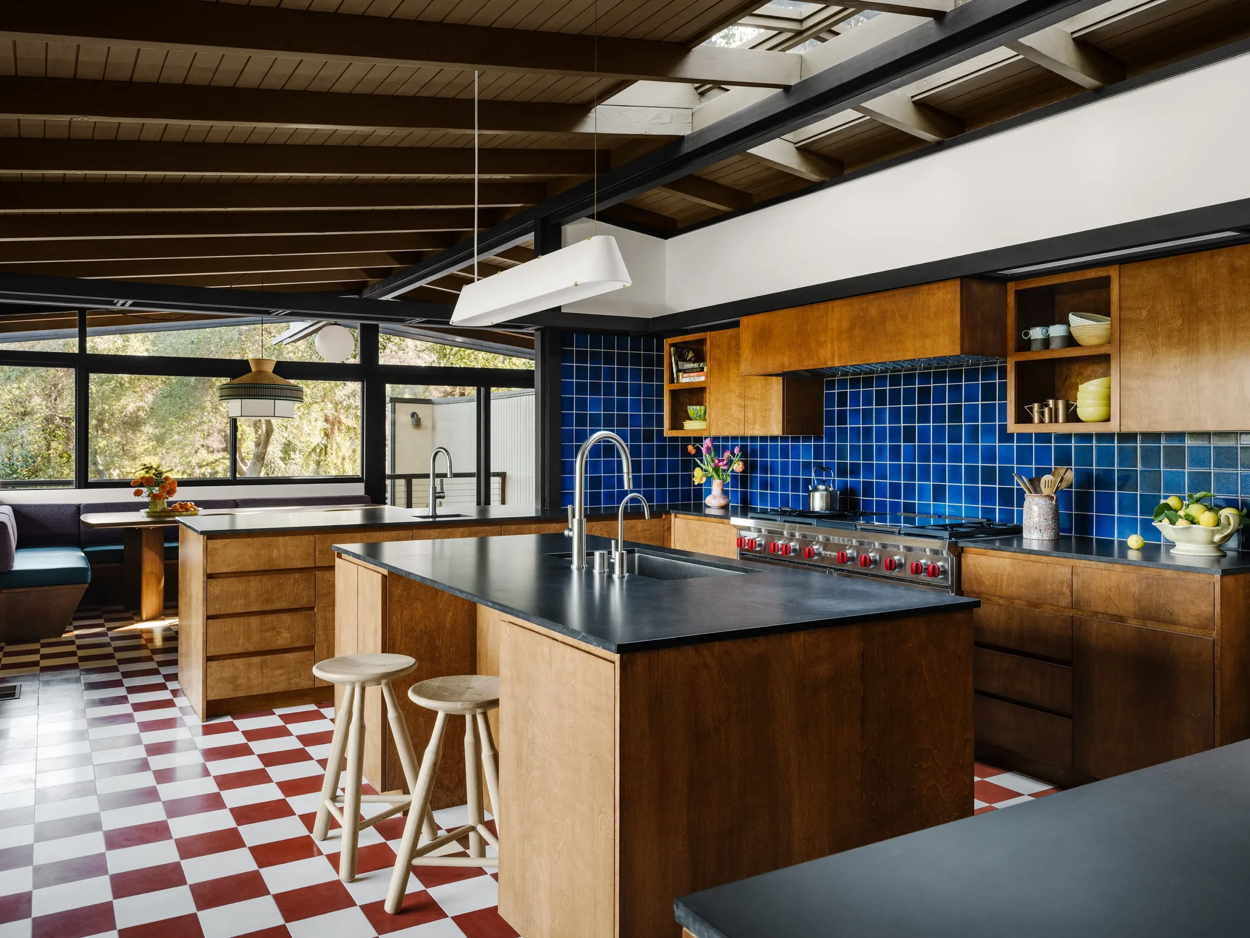 Mid-century modern kitchen with rich wood cabinetry, bold blue square tile backsplash, and red-and-white checkerboard flooring.