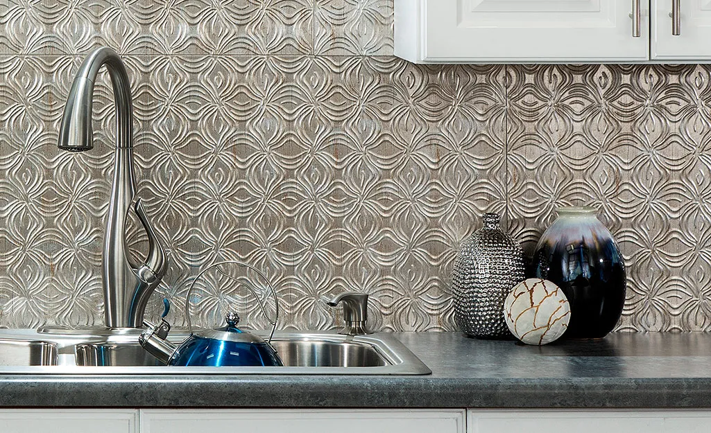 Modern kitchen backsplash with metallic textured panels behind a stainless steel sink and decorative ceramic vases.