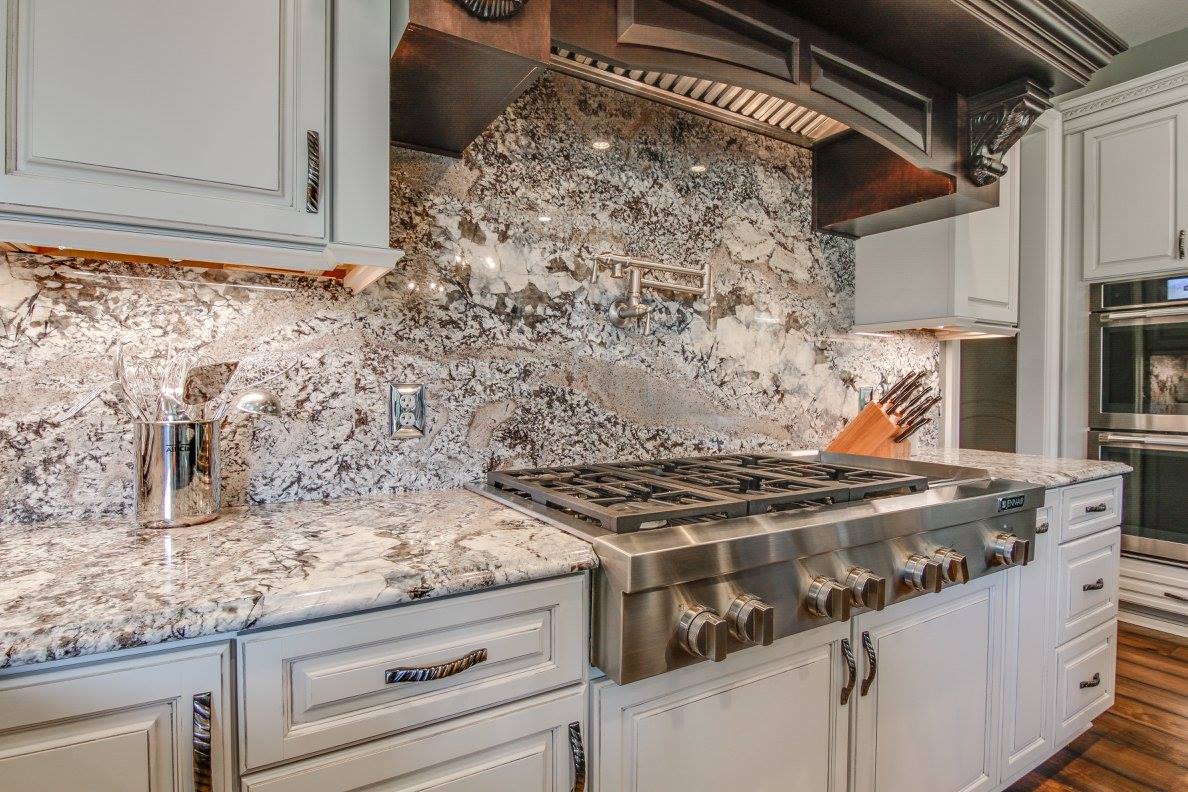 Stunning kitchen featuring a natural stone backsplash and granite countertops with a stainless steel gas range and custom white cabinetry.