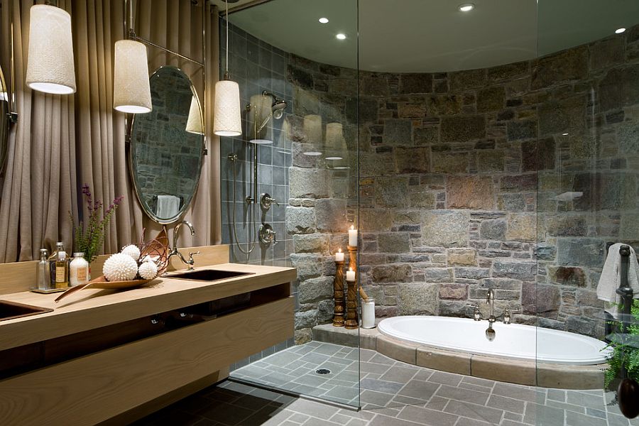 Elegant bathroom featuring a curved natural stone wall, sunken jacuzzi-style bathtub, and modern floating wood vanity with oval mirrors