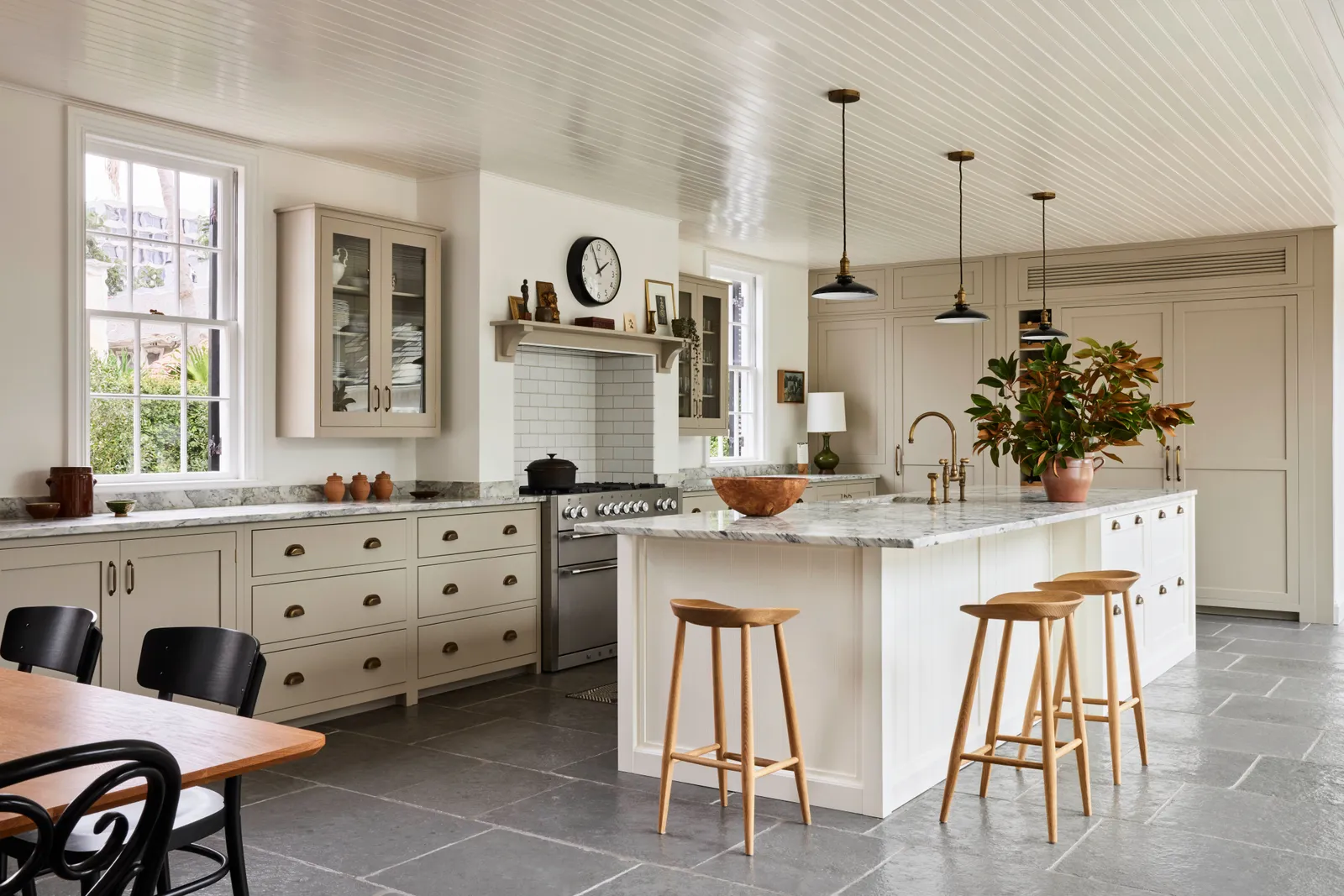 Traditional-style kitchen with cream cabinetry, marble countertops, and gray stone flooring, featuring a large island with wooden stools.