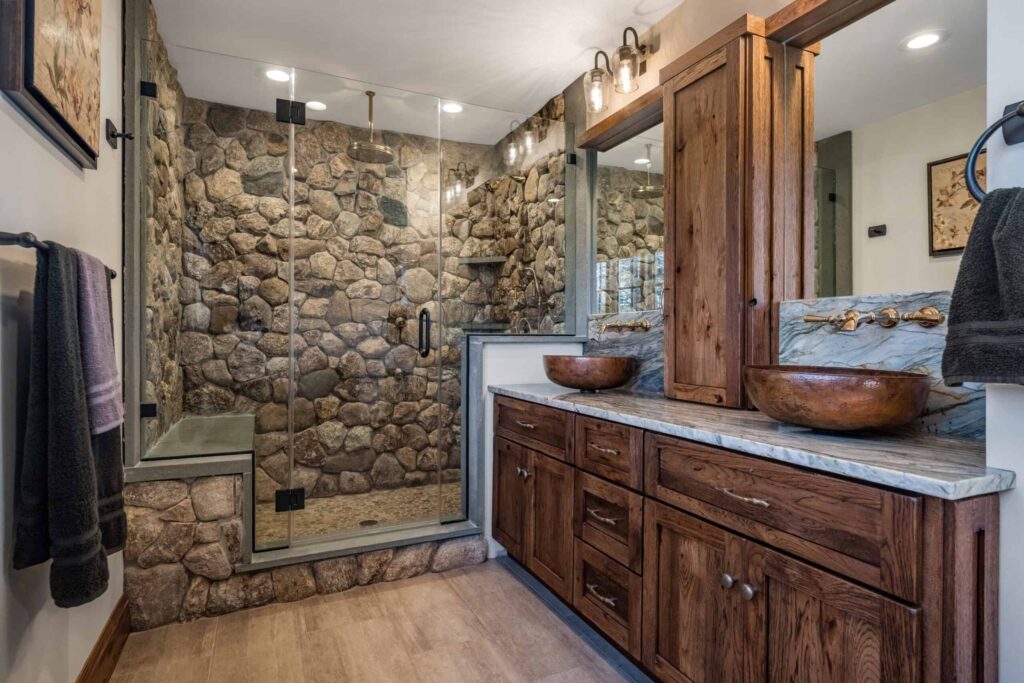 Rustic bathroom featuring a walk-in shower with natural stone walls, wooden double vanity, vessel sinks, and bronze fixtures
