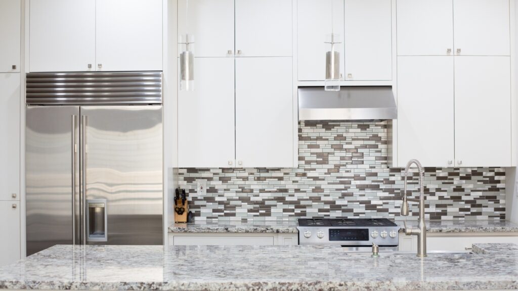 Contemporary kitchen featuring stainless steel appliances, white cabinets, mosaic tile backsplash, and granite countertops.