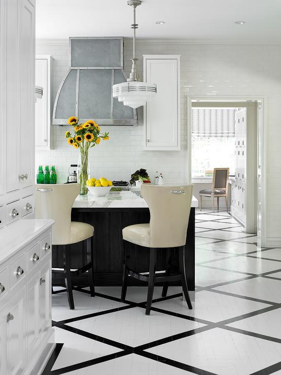 White kitchen with a zinc range hood, marble island, cream leather stools, and black lattice floor tile pattern