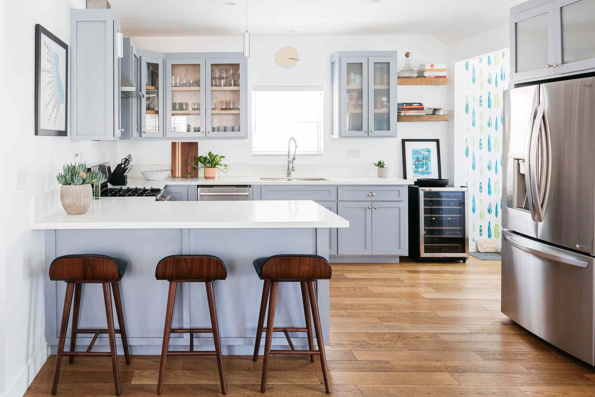 Contemporary kitchen with light blue cabinets, white countertops, wooden bar stools, and stainless steel appliances