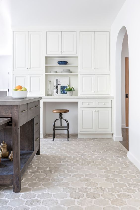 Kitchen with geometric light hexagon tile flooring, white built-in cabinets, a dark wood island, and a built-in desk nook