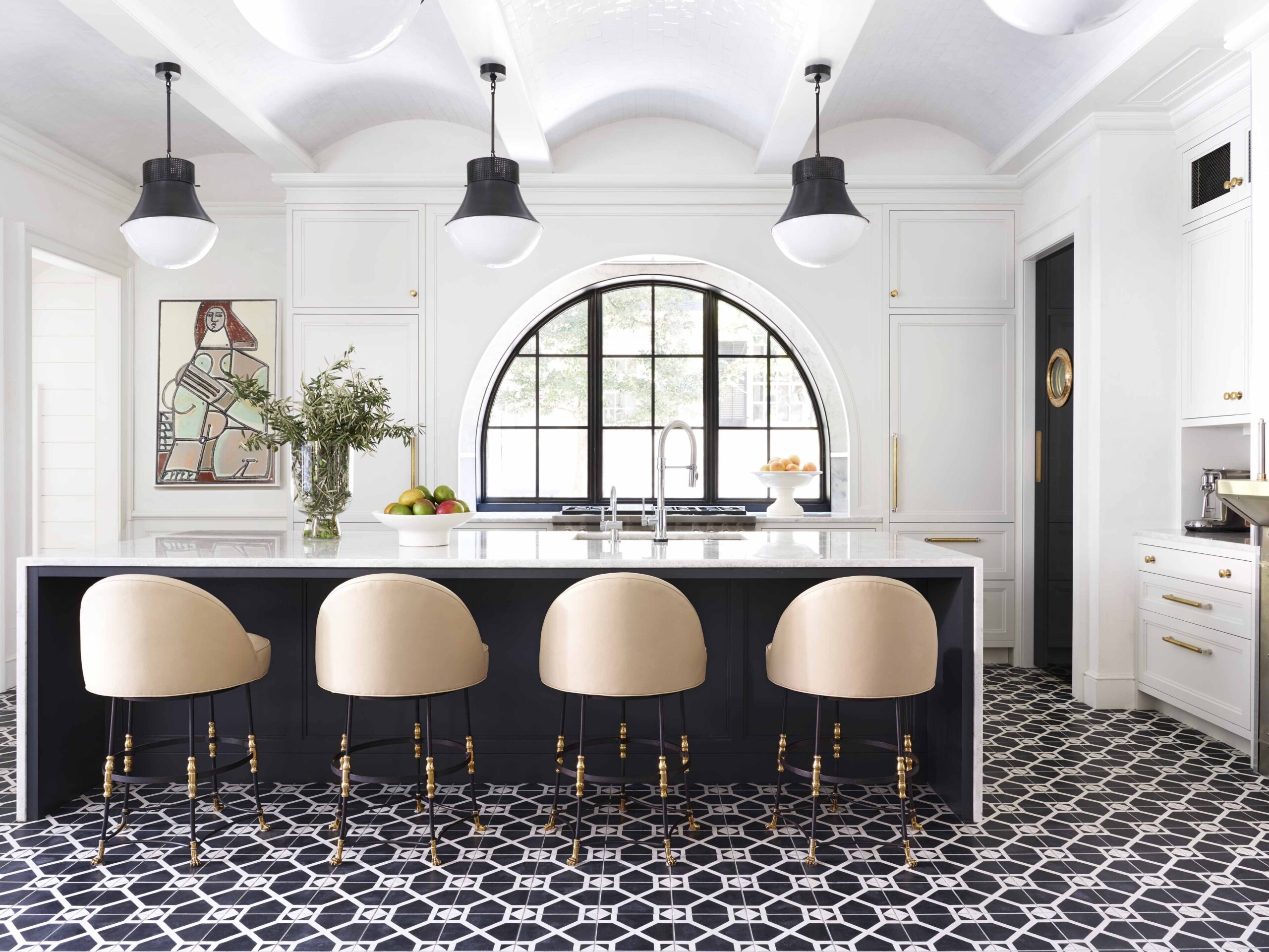 Luxurious kitchen featuring black-and-white geometric tile flooring, a large island with beige upholstered barstools, and a dramatic arched window.