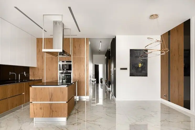 Modern kitchen with wood cabinetry, black countertops, and glossy marble-look tile flooring.