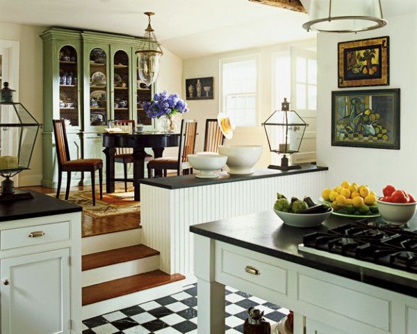 Traditional kitchen with black-and-white checkered floor, white cabinets, black countertops, and a raised dining area with green china cabinet.