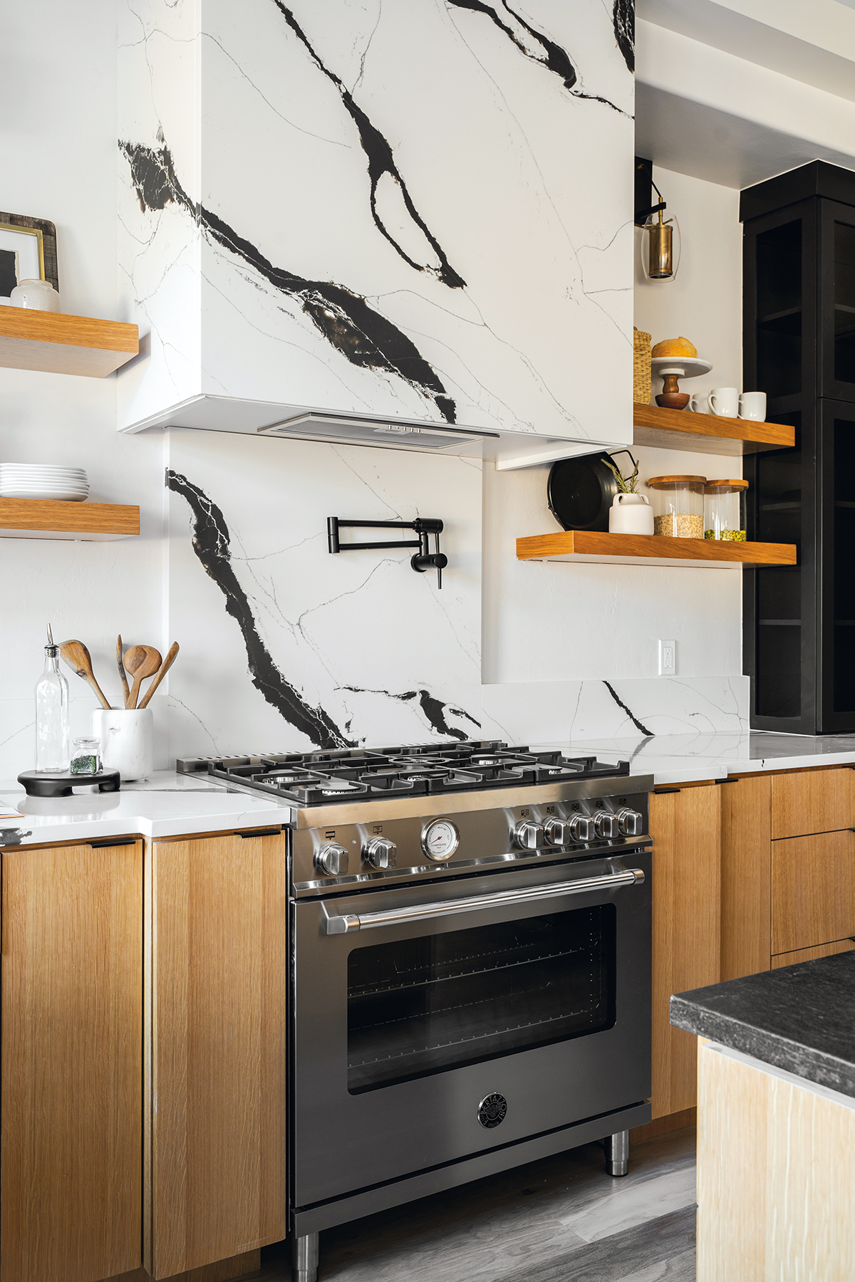 Modern kitchen with dramatic black and white marble backsplash and range hood, stainless steel stove, and light wood cabinetry.