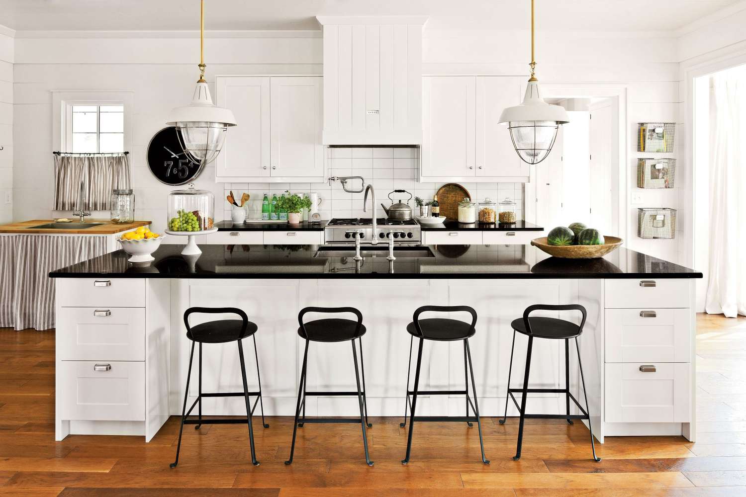 Bright white farmhouse kitchen with black countertops, industrial pendant lights, and wooden flooring.