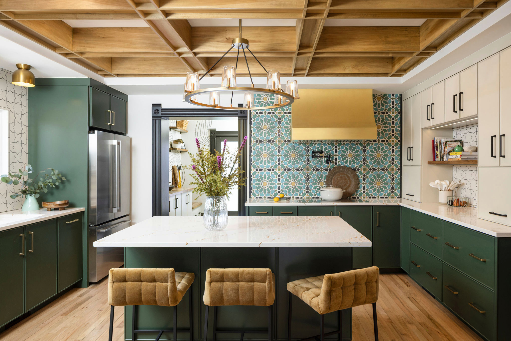Eclectic kitchen with green and cream cabinetry, bold patterned backsplash, and gold accents.