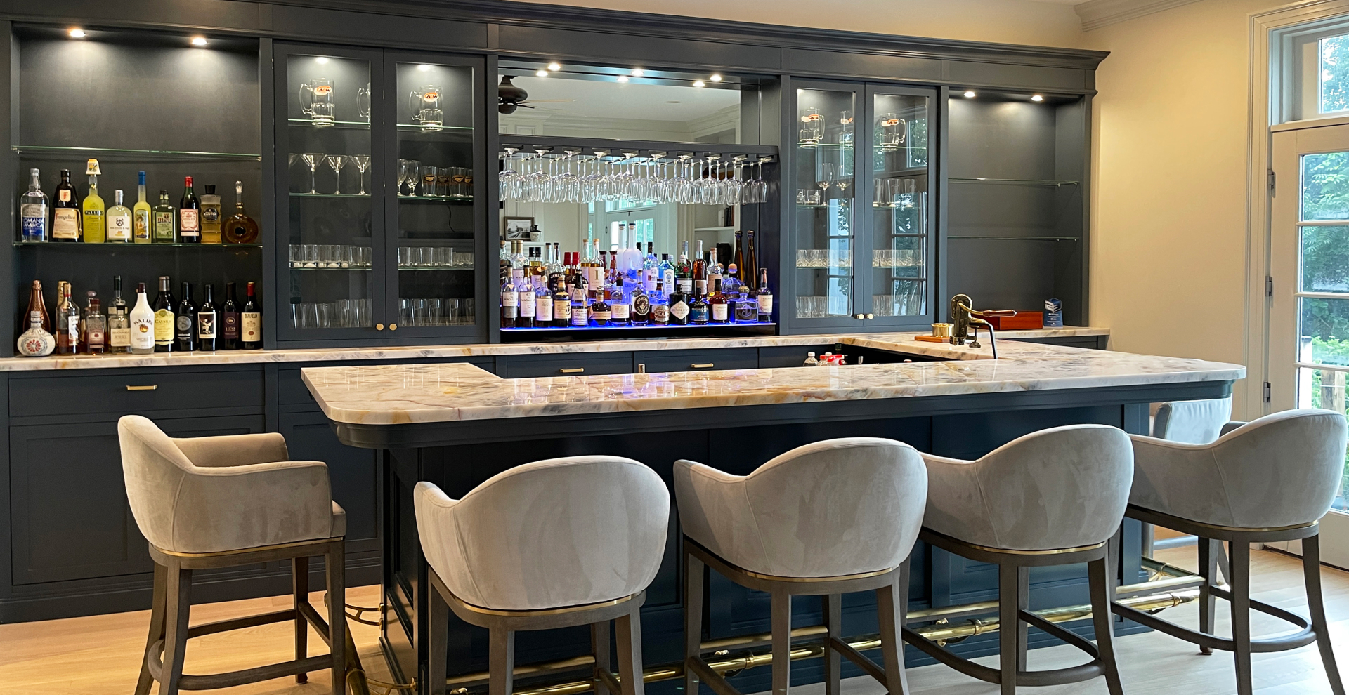 luxurious custom home bar with blue cabinetry, marble countertop, and plush velvet bar stools