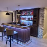 modern home bar with dark wood cabinetry, stone backsplash, and illuminated liquor shelves