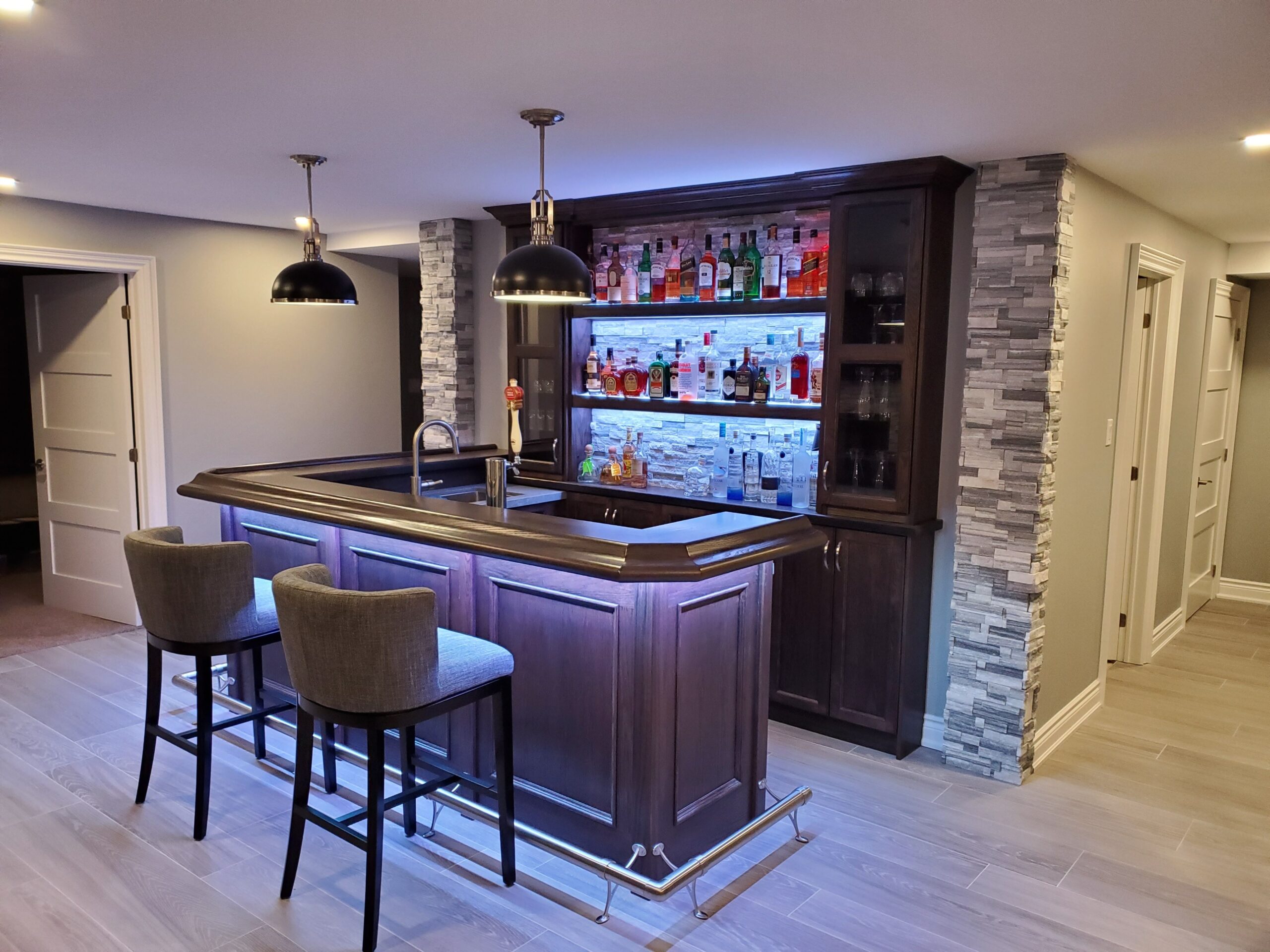 modern home bar with dark wood cabinetry, stone backsplash, and illuminated liquor shelves