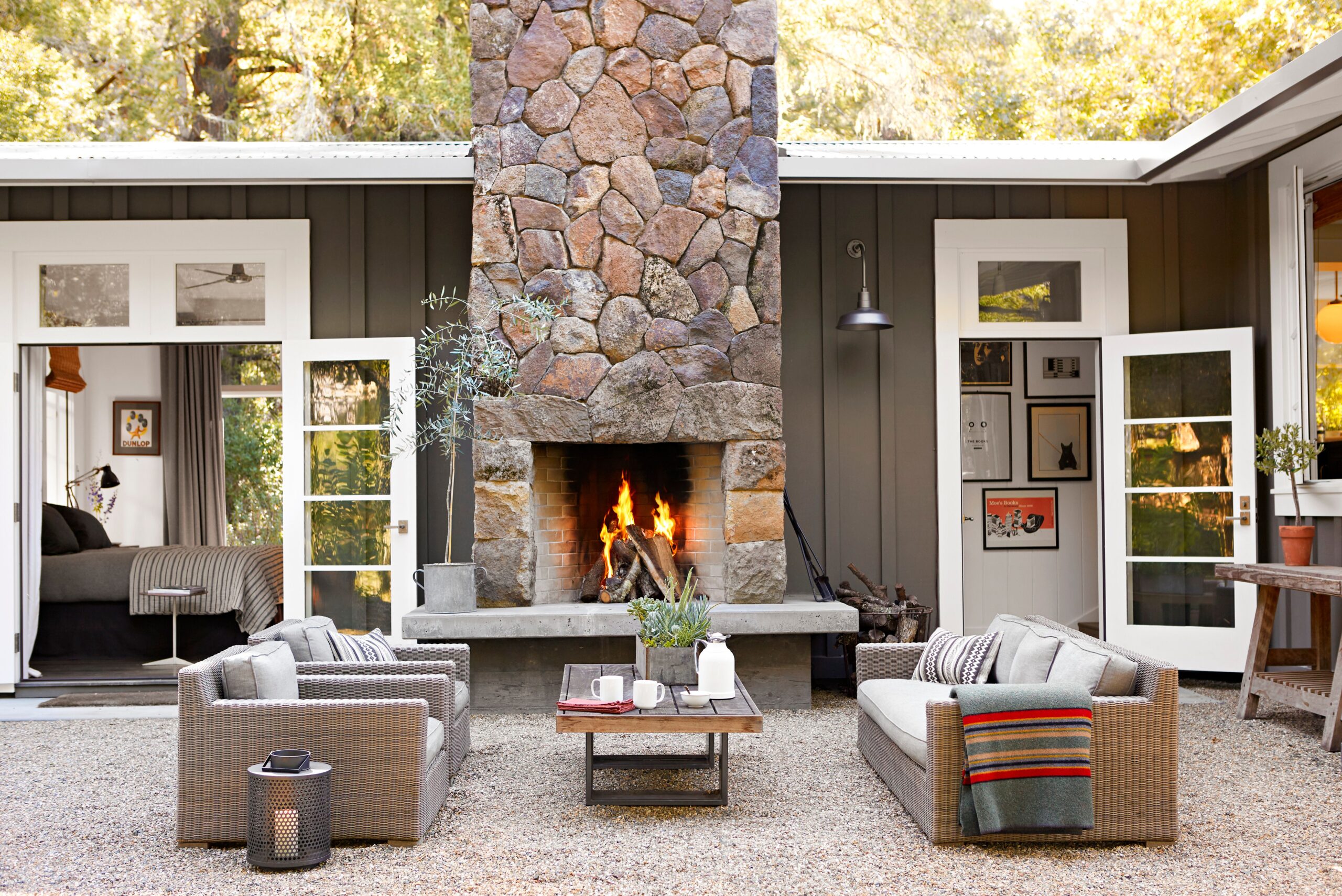 Cozy outdoor patio with stone fireplace, wicker sofas, and gravel floor surrounded by a modern dark exterior home.