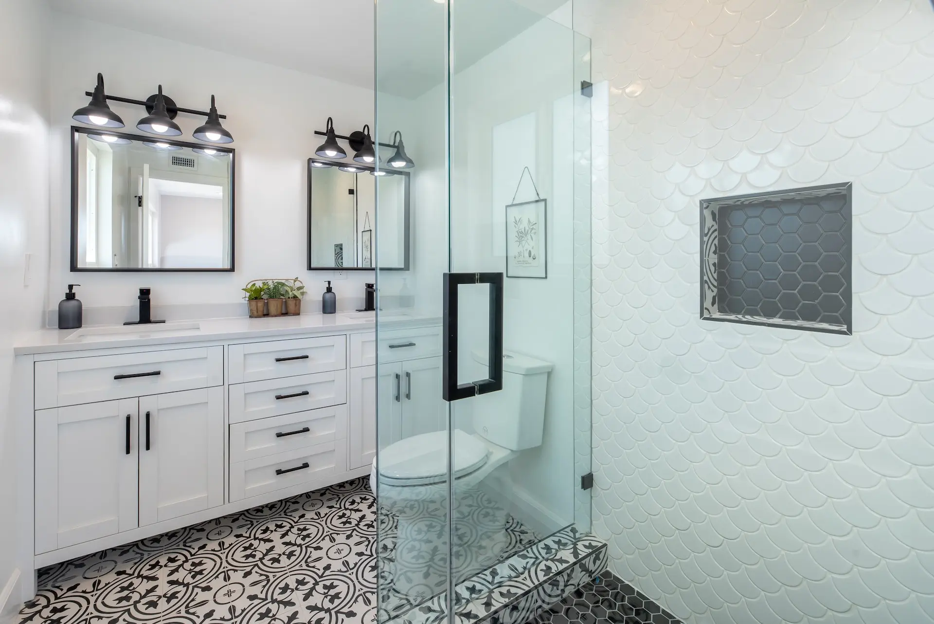 A modern bathroom featuring a double vanity with black fixtures, a glass shower with a white and black patterned floor, and sleek decor.