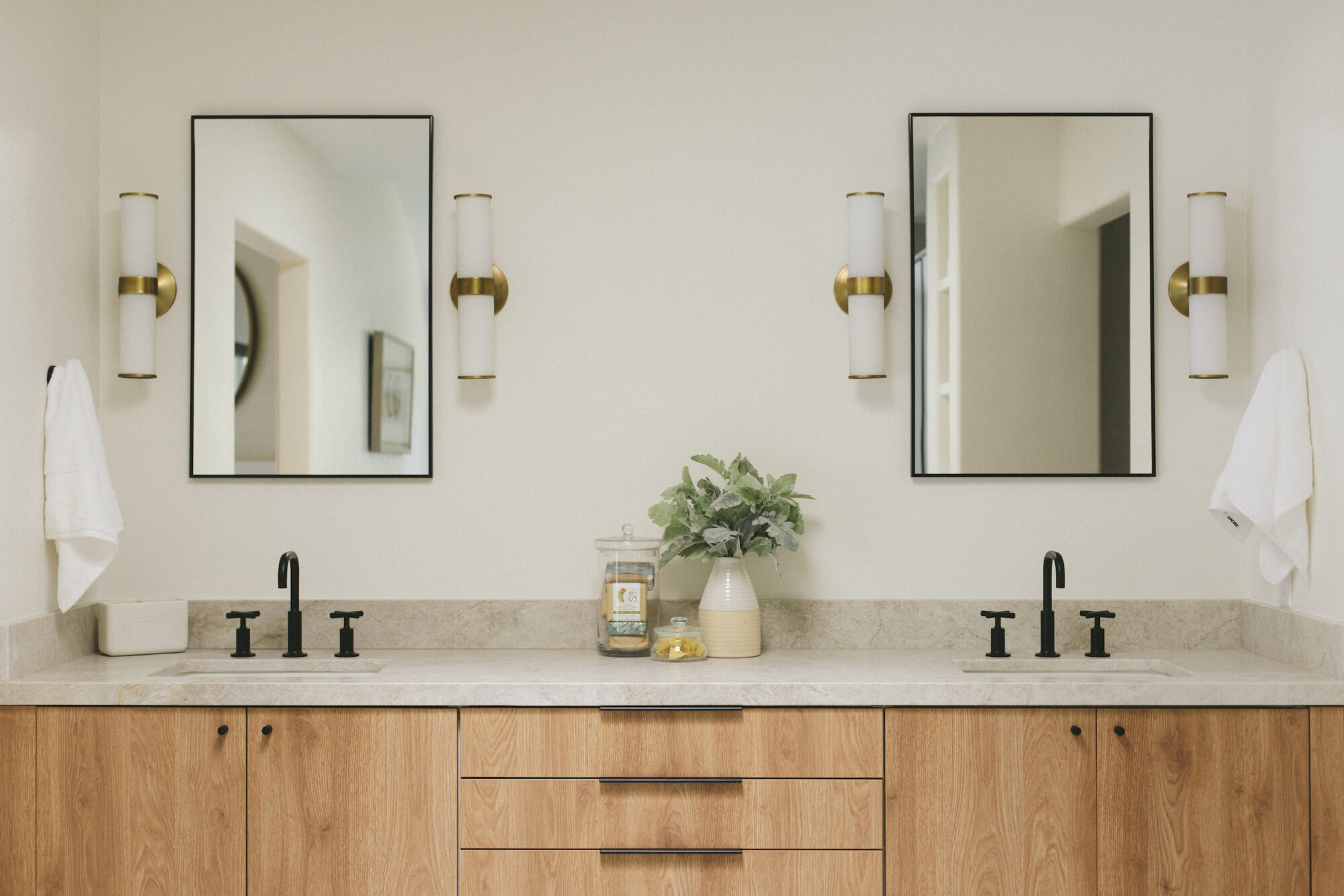 Modern bathroom with natural wood vanity, black faucets, and brass lighting fixtures.