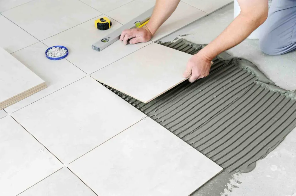 Person laying ceramic floor tiles using adhesive mortar.