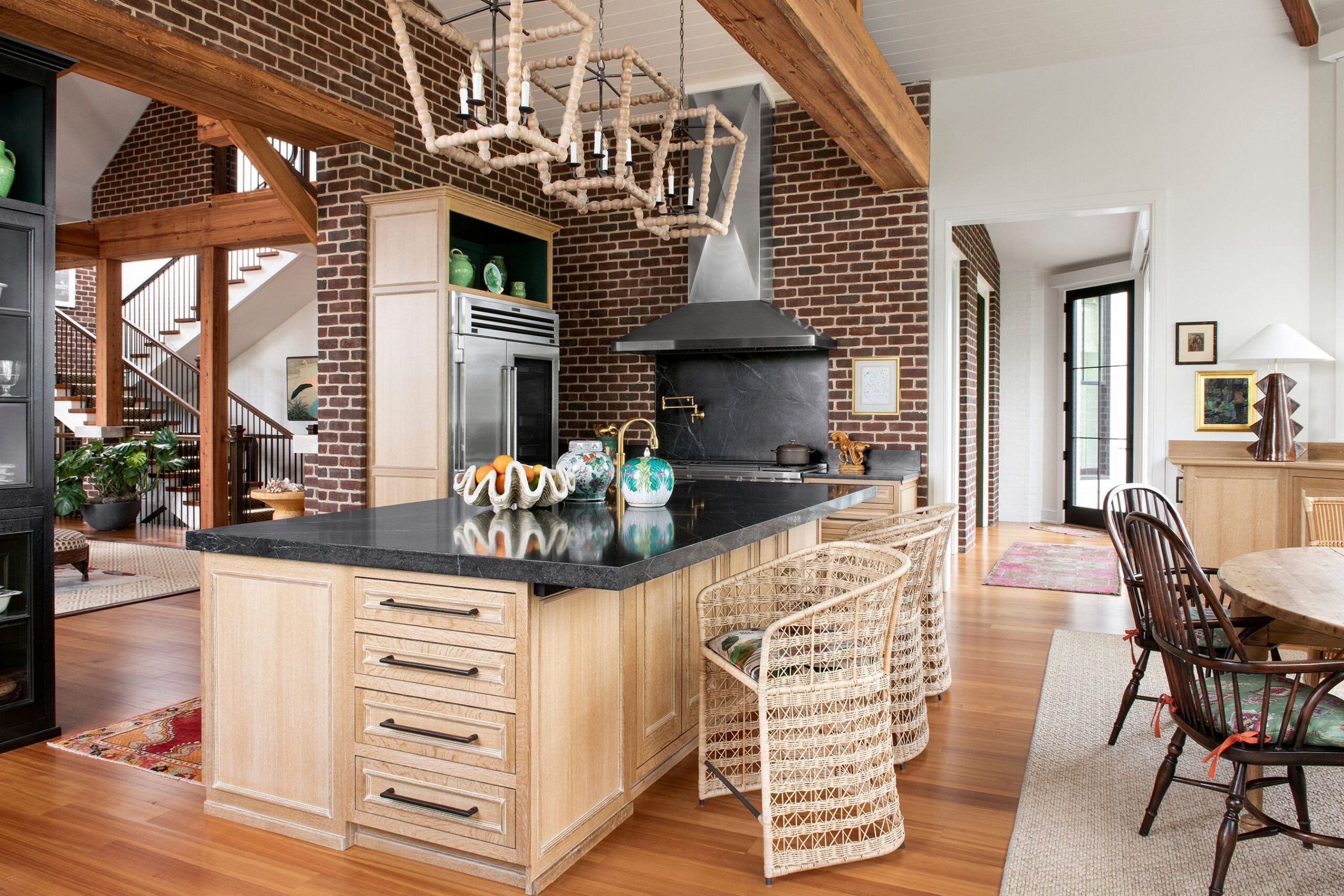 Eclectic kitchen with exposed brick walls, light wood cabinetry, black stone countertops, and wicker bar stools.