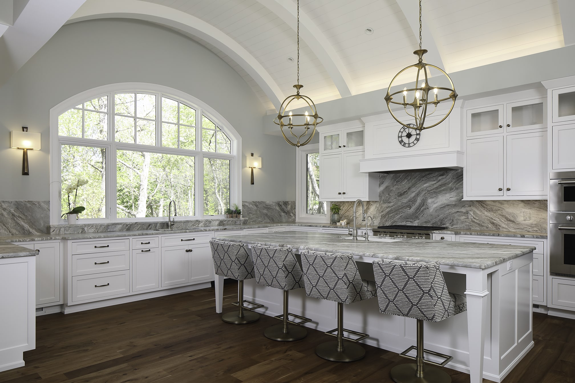 Elegant kitchen with vaulted ceiling, large arched window, marble countertops, and white cabinets