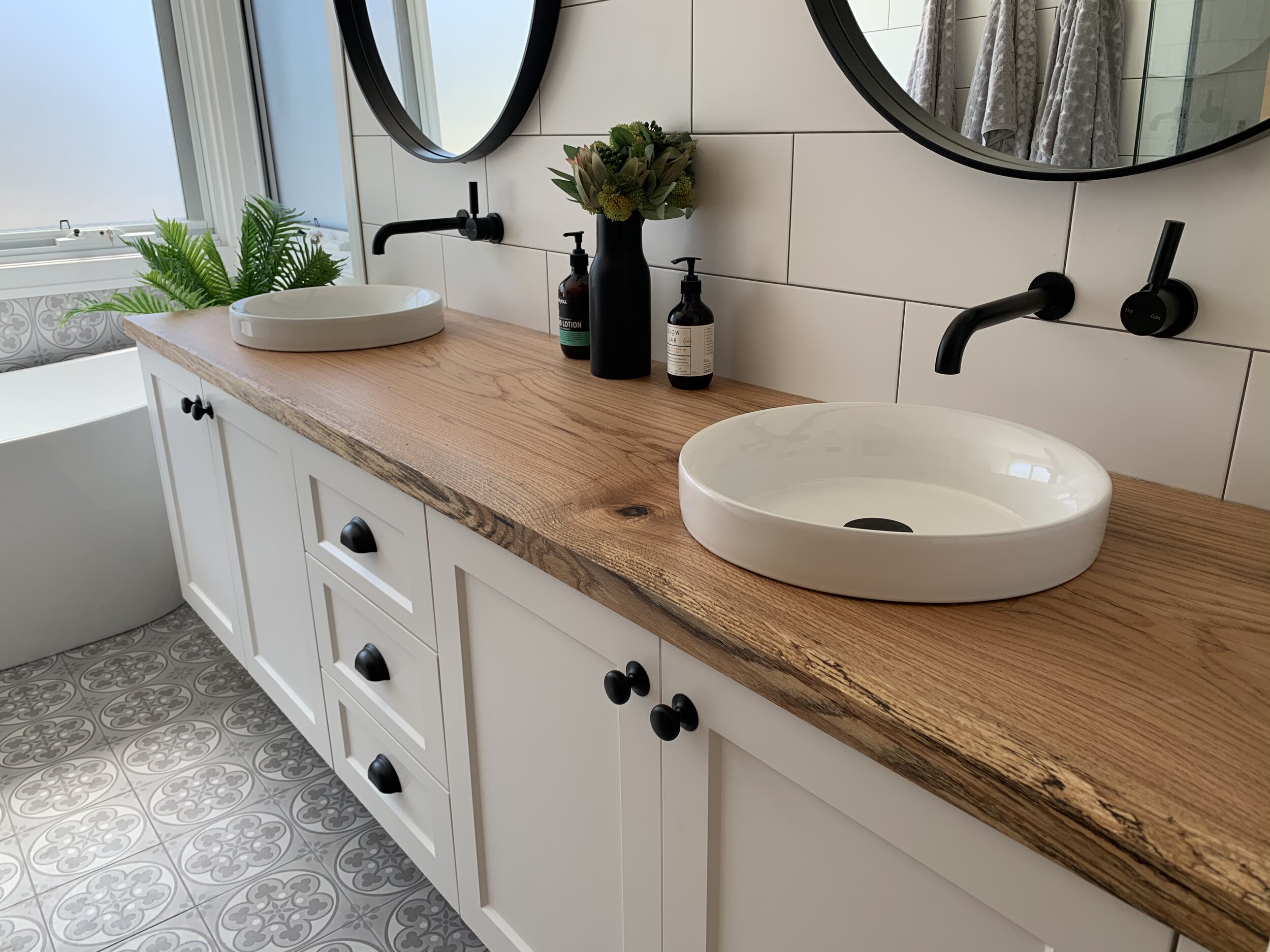 Modern bathroom with oak wood countertop, black fixtures, and round mirrors.
