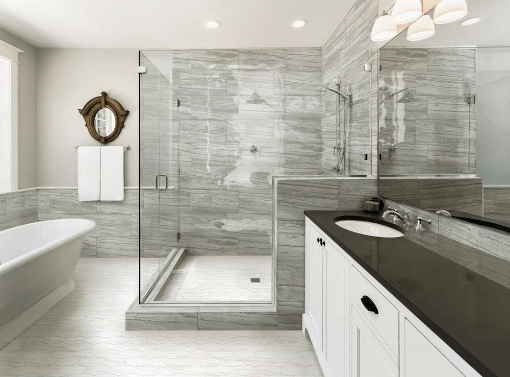 Modern bathroom with glass shower enclosure, gray marble walls, black countertop, and a freestanding bathtub.