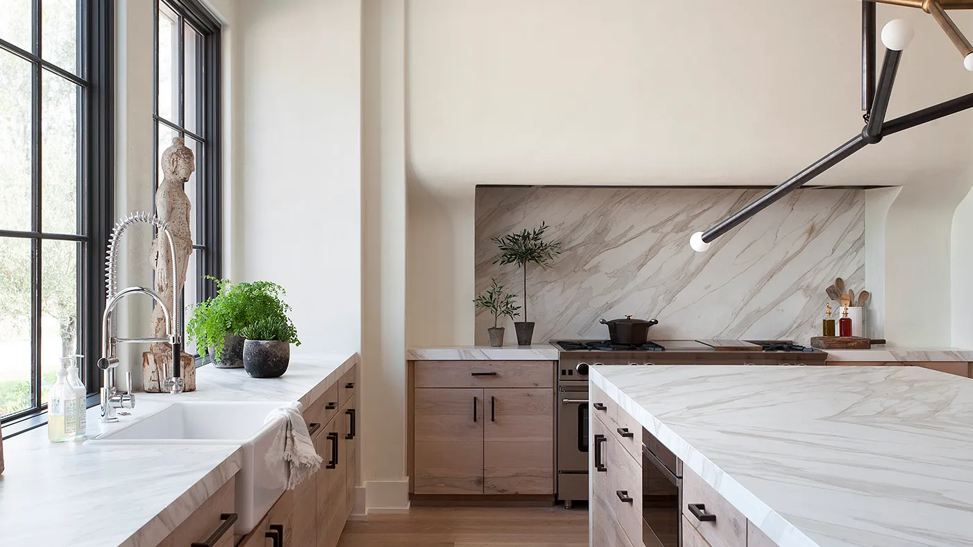 Modern kitchen with marble countertops and backsplash featuring light wood cabinets