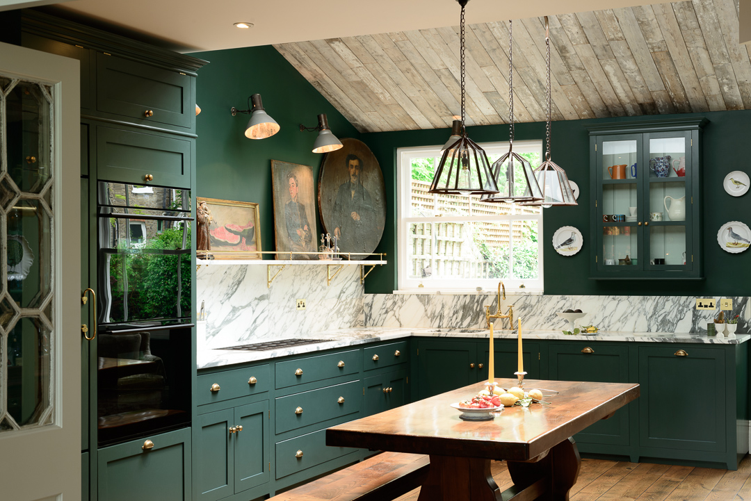 Vintage-style kitchen with dark green cabinets, marble countertops, and rustic wooden dining table.