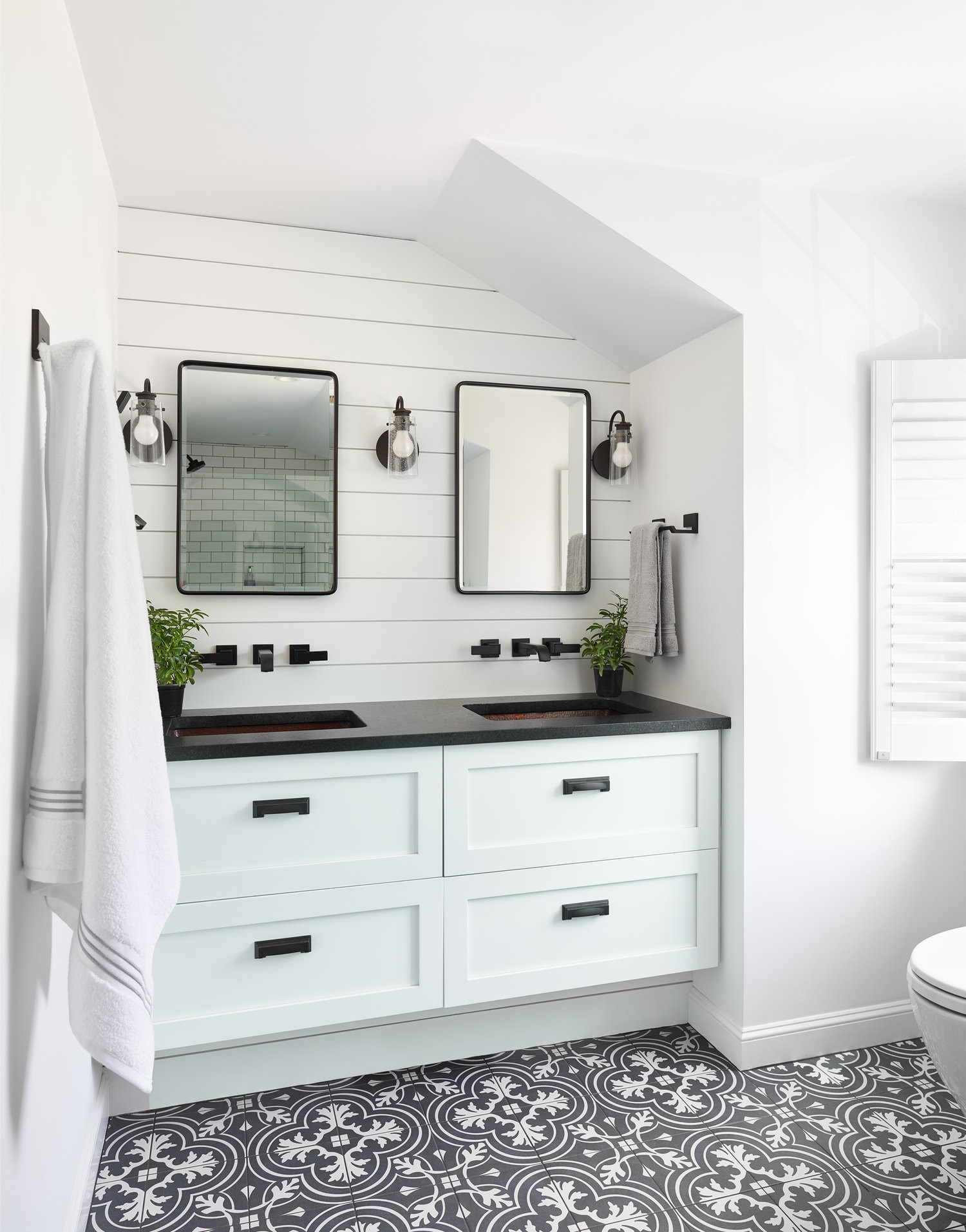 Modern bathroom design with double mirrors, black fixtures, and intricate patterned floor tiles.