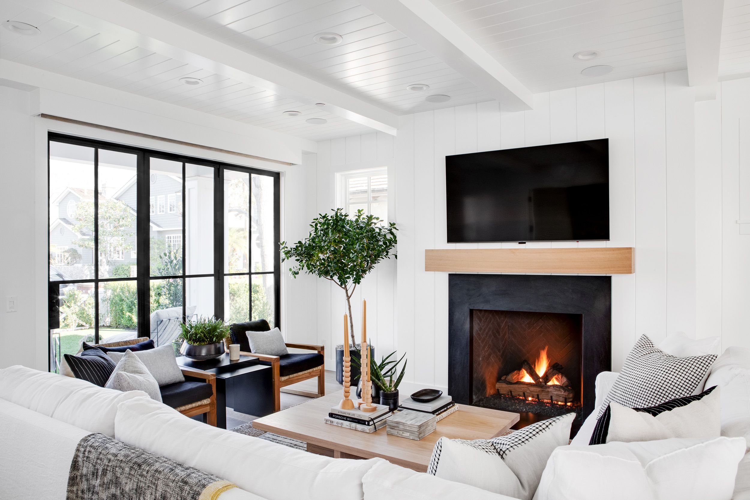 Bright modern living room with white shiplap walls, black fireplace, wood mantel, and large windows.