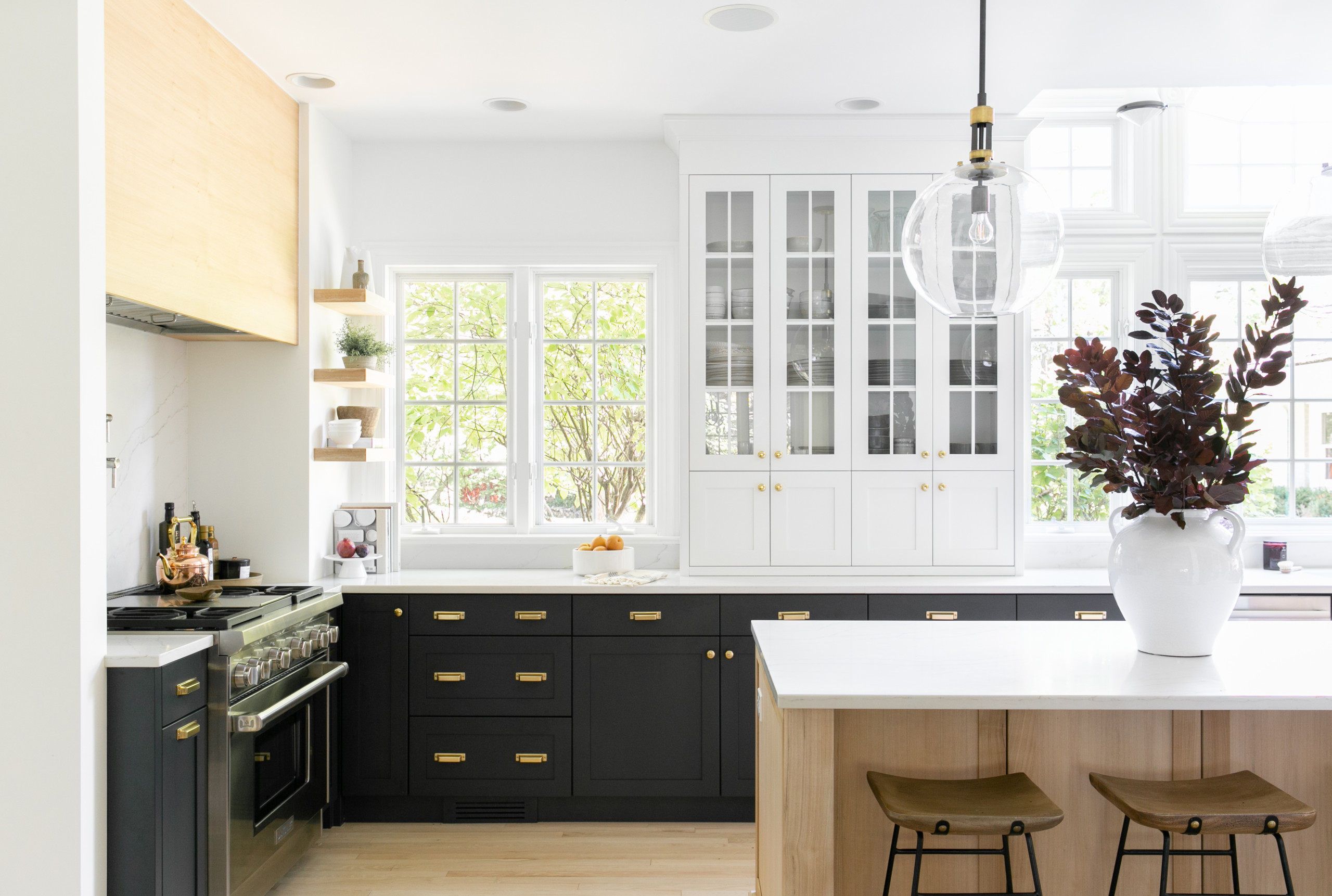 Modern kitchen with black lower cabinets, white upper cabinets with glass doors, and natural wood accents.