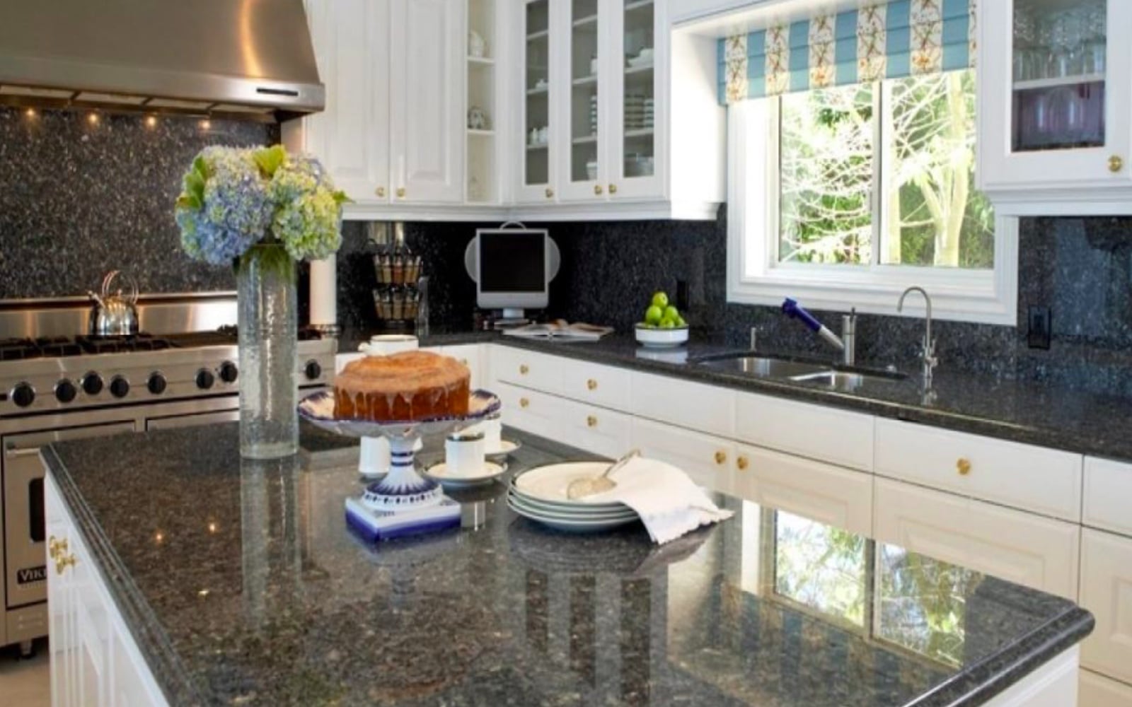 Modern kitchen with glossy black granite countertops, white cabinets, stainless steel stove, and large center island decorated with flowers and cake.